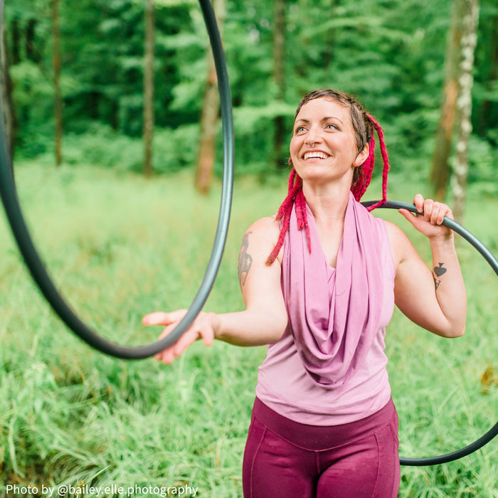 Smiling hoop dancer spinning two polypro hula hoops in a grassy field