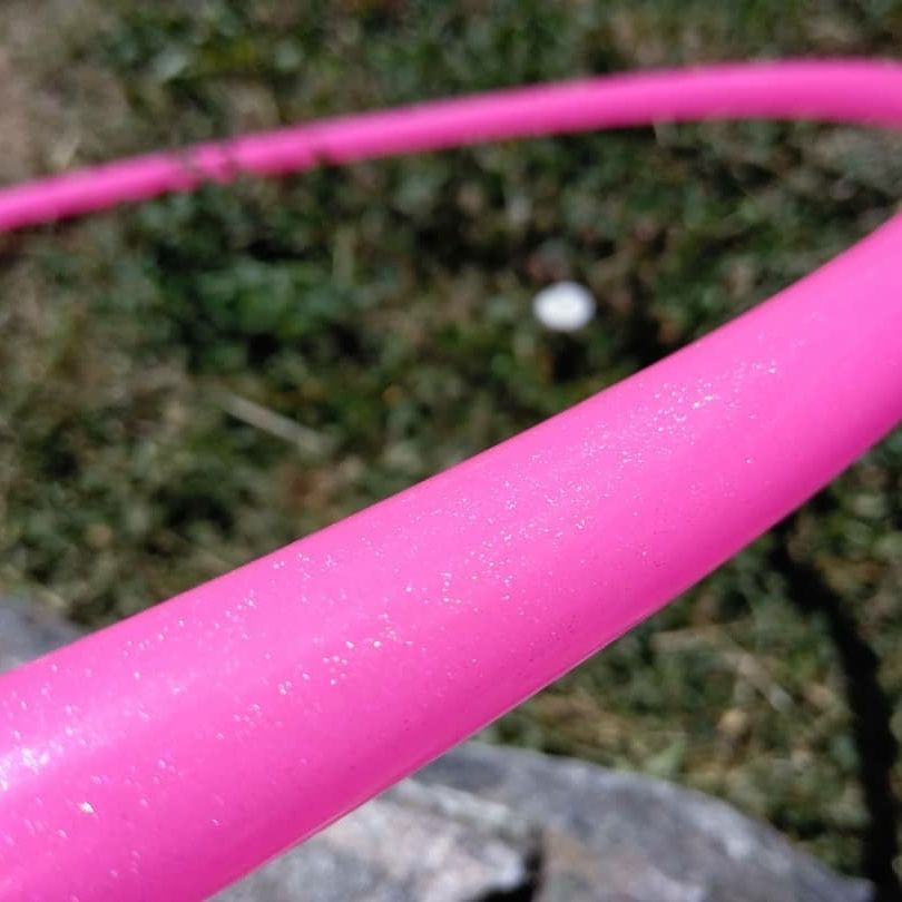 Close-up of a pink hula hoop with glittery texture against a blurred natural background