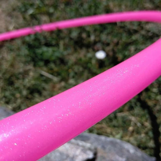 Close-up of a pink hula hoop with glittery texture against a blurred natural background